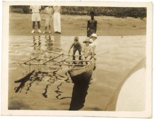 Photograph depicting children pushing an outrigger canoe into the water