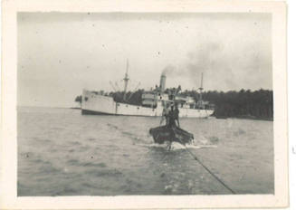 Photograph depicting a small boat being towed and large vessel in background