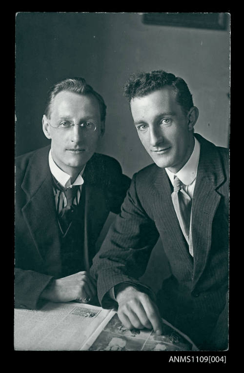 Photographic postcard of two men wearing suits and looking directly into the camera