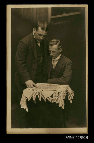 Photographic postcard of two men at a small table reading a 'The Daily Mirror' newspaper