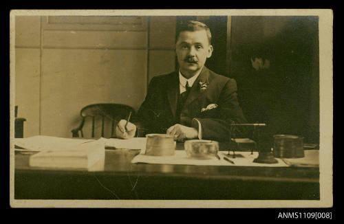 Photographic postcard of a man seated at a desk