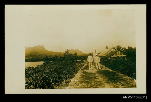 Photographic postcard two men standing in white suits on a path that leads to a white house