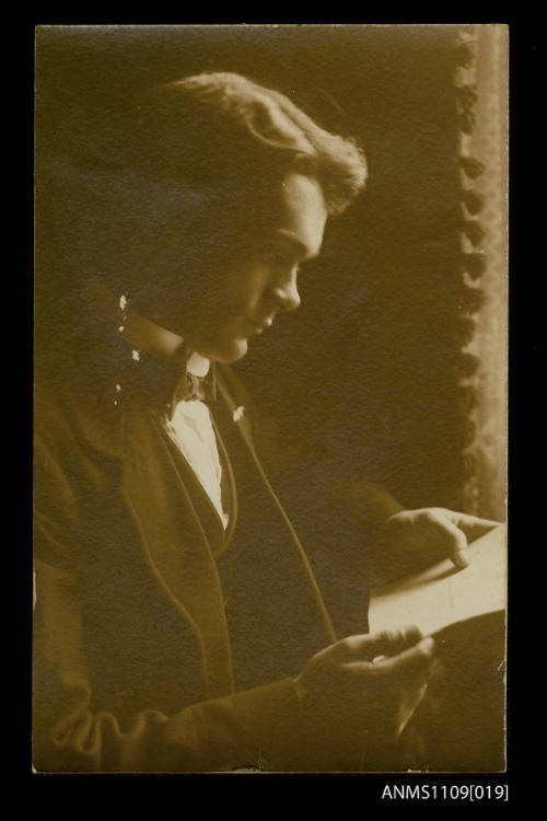 Photographic postcard of a portrait of a young man reading