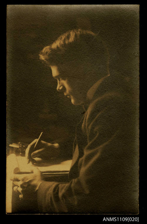 Photographic postcard of a portrait of a young man writing