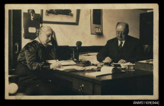 Photographic postcard of a man and a woman seated at a partners desk