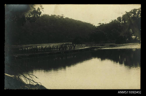 Photographic postcard of men standing on a low bridge across a river