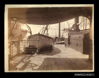 Deck of unknown ship with canvas awning above and life boat in davits to left