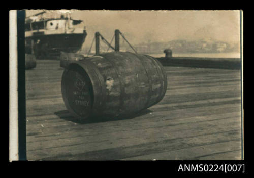 Photograph at centre wooden barrel on pier on side at end printing diamond logo, also "Suva Fiji  via Sydney"