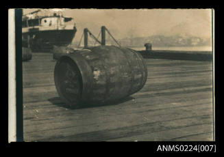 Photograph at centre wooden barrel on pier on side at end printing diamond logo, also "Suva Fiji  via Sydney"