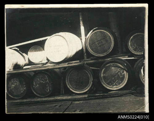 Two rows of barrels stacked on side in two layers circa four above and five below, Some barrels have white numbers on ends