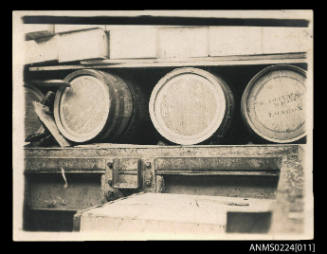 Photograph of three barrels stacked in hull of ship