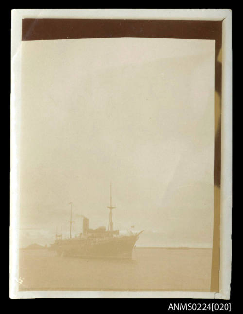 Faded photograph from bow and starboard view of single funnel steamer, two masts, anchored