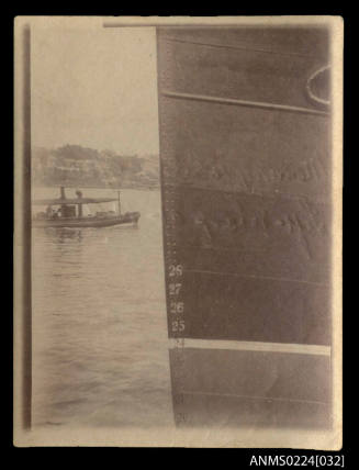 Photograph, right half of picture port bow of ship, metal hull centre left, small single open deck vessel, canvas awning above, partial starboard view