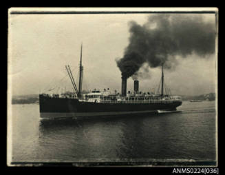 Port and bow view of twin funnel cargo passenger ship under way dark funnels, fore funnel belching black smoke.