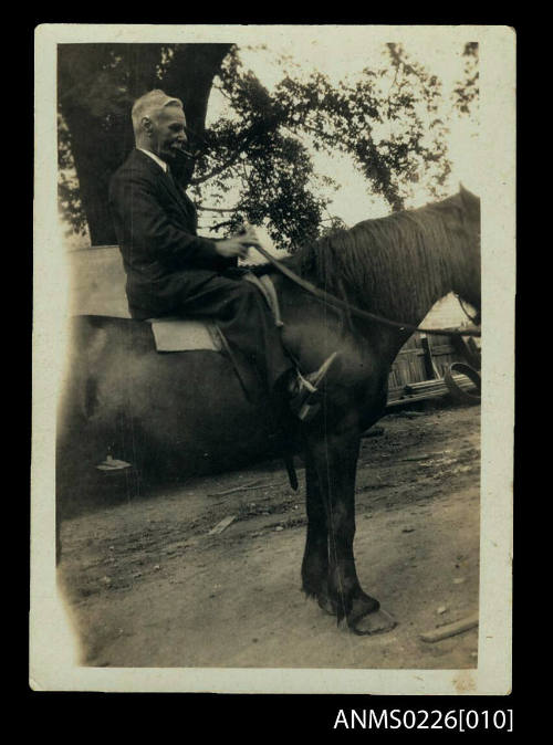 Man seated on horse. Man wears dark suit, white collar, has grey hair and moustache. Smokes pipe, Captain mckilliam