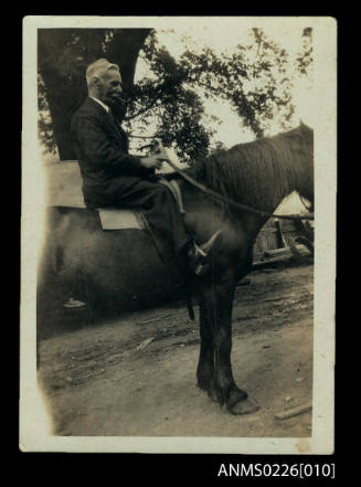 Man seated on horse. Man wears dark suit, white collar, has grey hair and moustache. Smokes pipe, Captain mckilliam