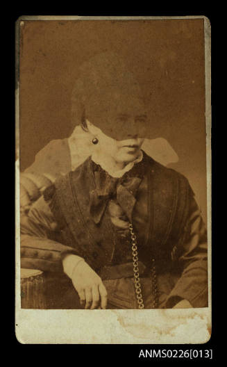 Portrait of adult female seated and wears a scarf over jacket and a long chain from her neck, ear ring visible on right ear and rigth arm on rest, Mrs McKilliam, snr