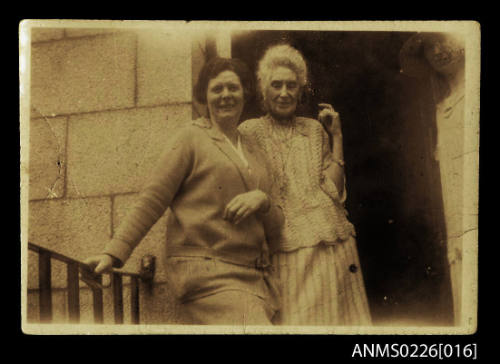 Two women on stairs at door of stone building