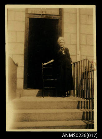 Elderly lady, dark dress, grey hair left hand on railing of steps