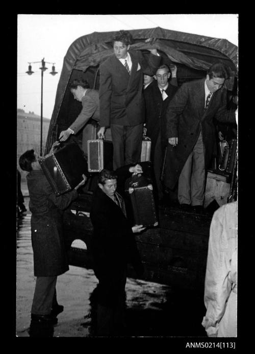 Migrants with luggage on tarpaulin covered truck