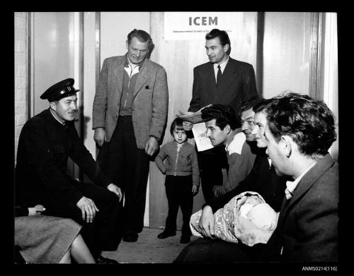 Migrants in an office talk to a uniformed official