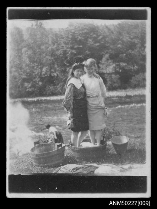 Two women standing in wooden tub of washing