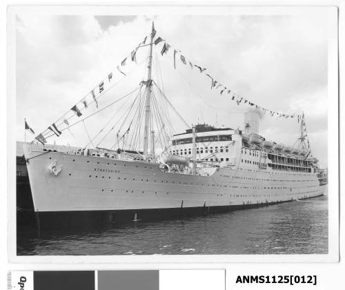 P&O passenger liner STRATHAIRD moored starboard side to wharf and dressed with flags and what is possibly a paying-off pennant flying from the mast at the stern.