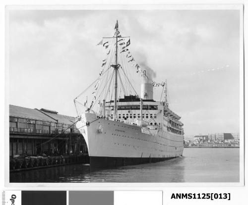 P&O passenger liner STRATHAIRD moored starboard side to wharf and dressed with flags and what is possibly a paying-off pennant flying from the mast at the stern.