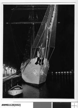 A night time image of ESMERALDA, a four-masted barquentine tall ship of the Chilean Navy, moored in Sydney Cove with a moored lifeboat in the foreground.