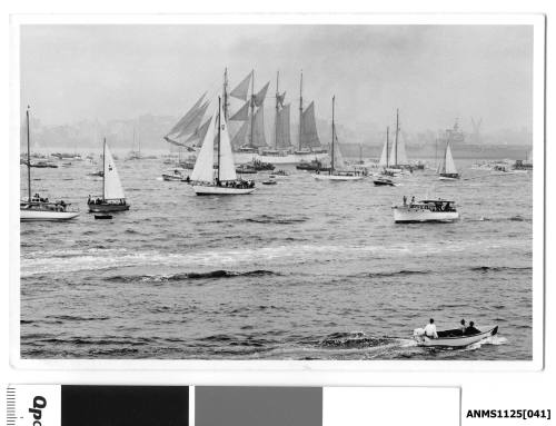 ESMERALDA, a four-masted barquentine of the Chilean Navy, arriving in Sydney Harbour escorted by many small craft including a small open power boat.